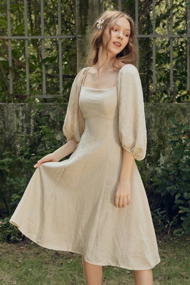 a woman in a beige dress posing for the camera with her hand on her hip