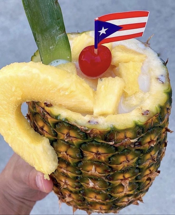 a person holding up a pineapple with a cherry on top and an american flag in the middle