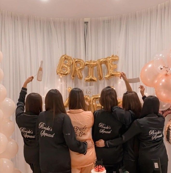 three women standing in front of a sign that says bride and groom with balloons behind them