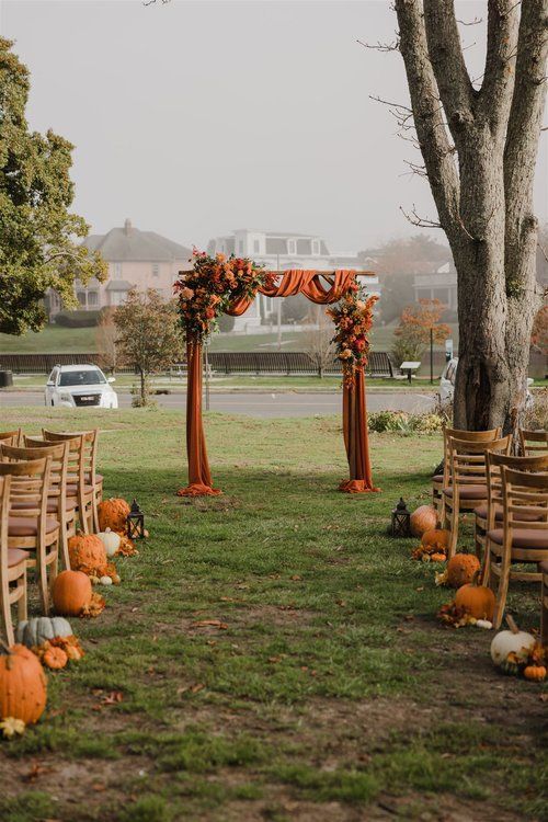 an outdoor ceremony set up with wooden chairs and pumpkins on the grass in front of a tree