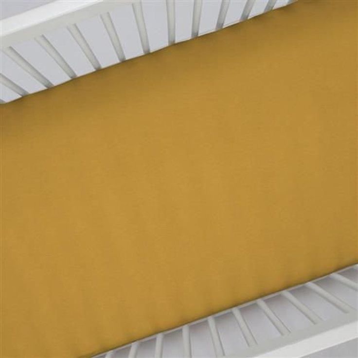 a crib bed with yellow sheets and white rails