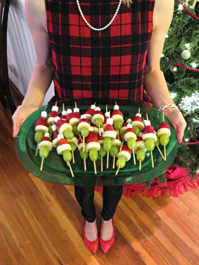 a woman holding a platter with apples and marshmallows on it in front of a christmas tree