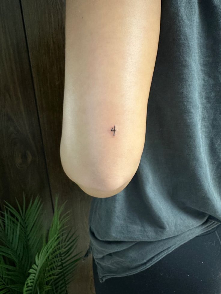 a person with a small cross tattoo on their left arm, and a potted plant in the background