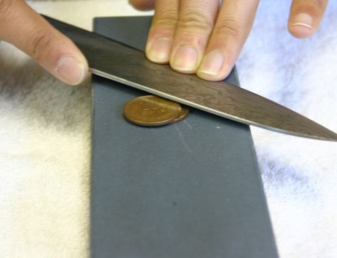 a person holding a knife over a piece of paper with a penny on the side