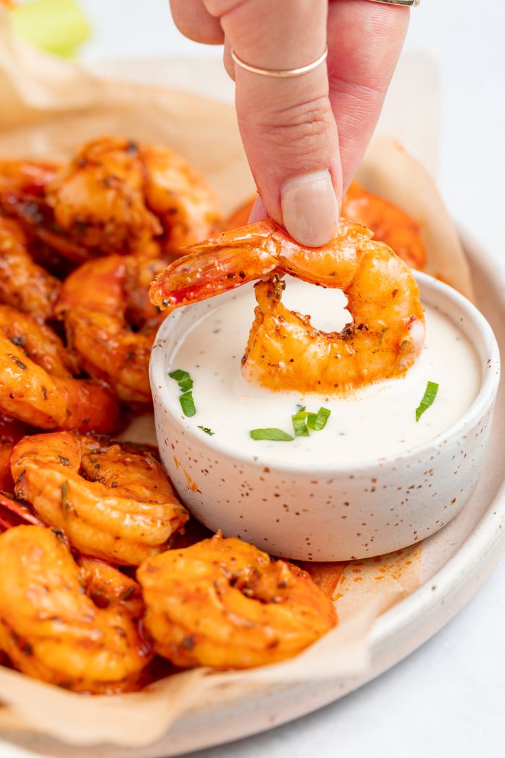 a person dipping shrimp into a small bowl