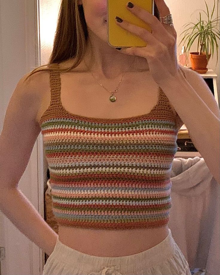 a woman taking a selfie with her cell phone wearing a crocheted crop top