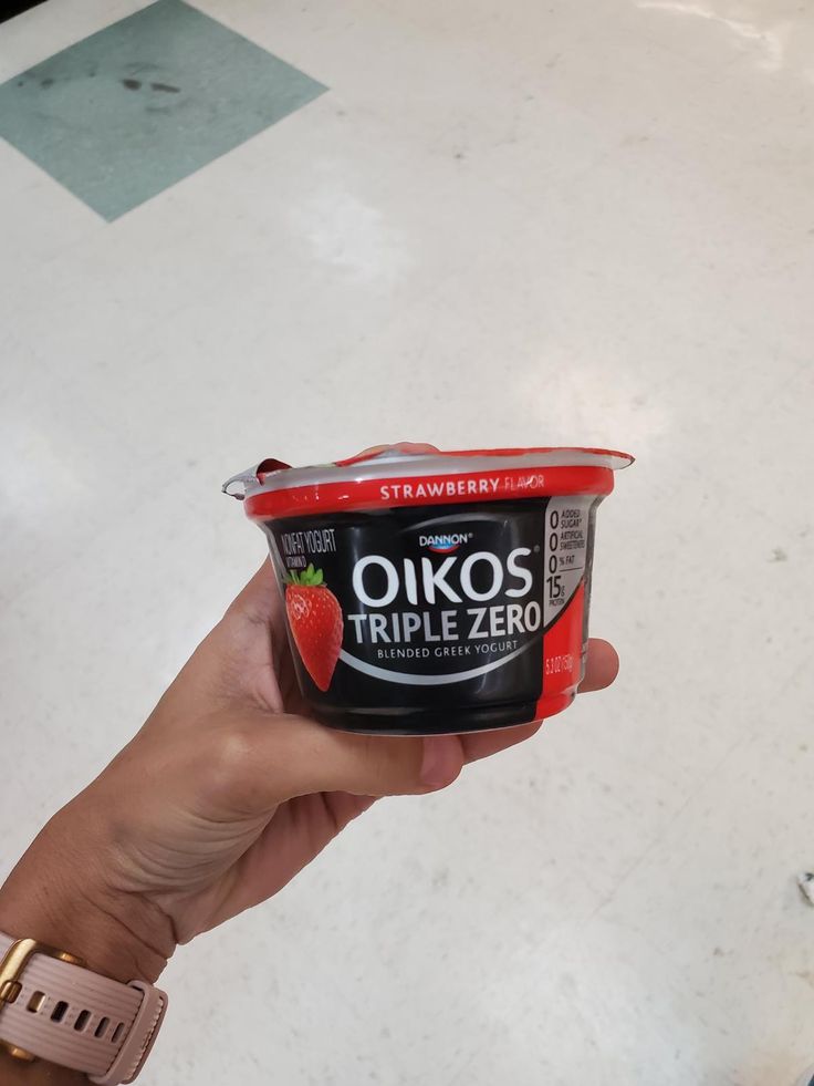 a hand holding up a yogurt in a container with strawberries on top