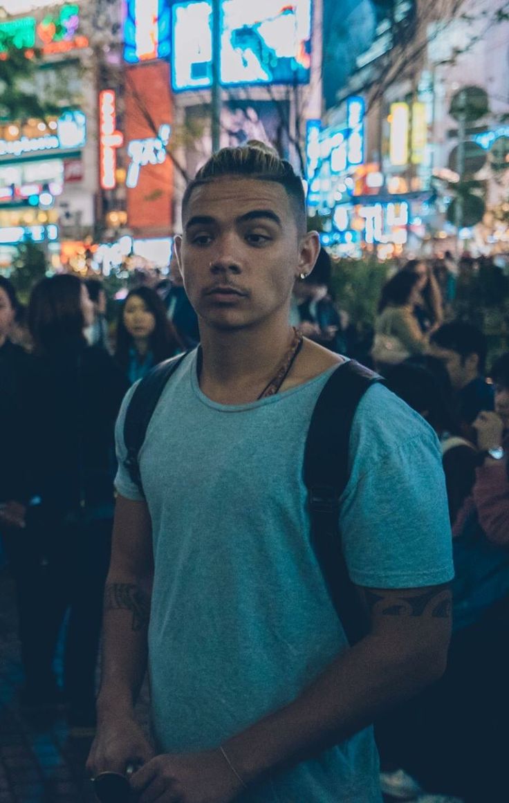 a young man standing in the middle of a crowded street at night with people walking around