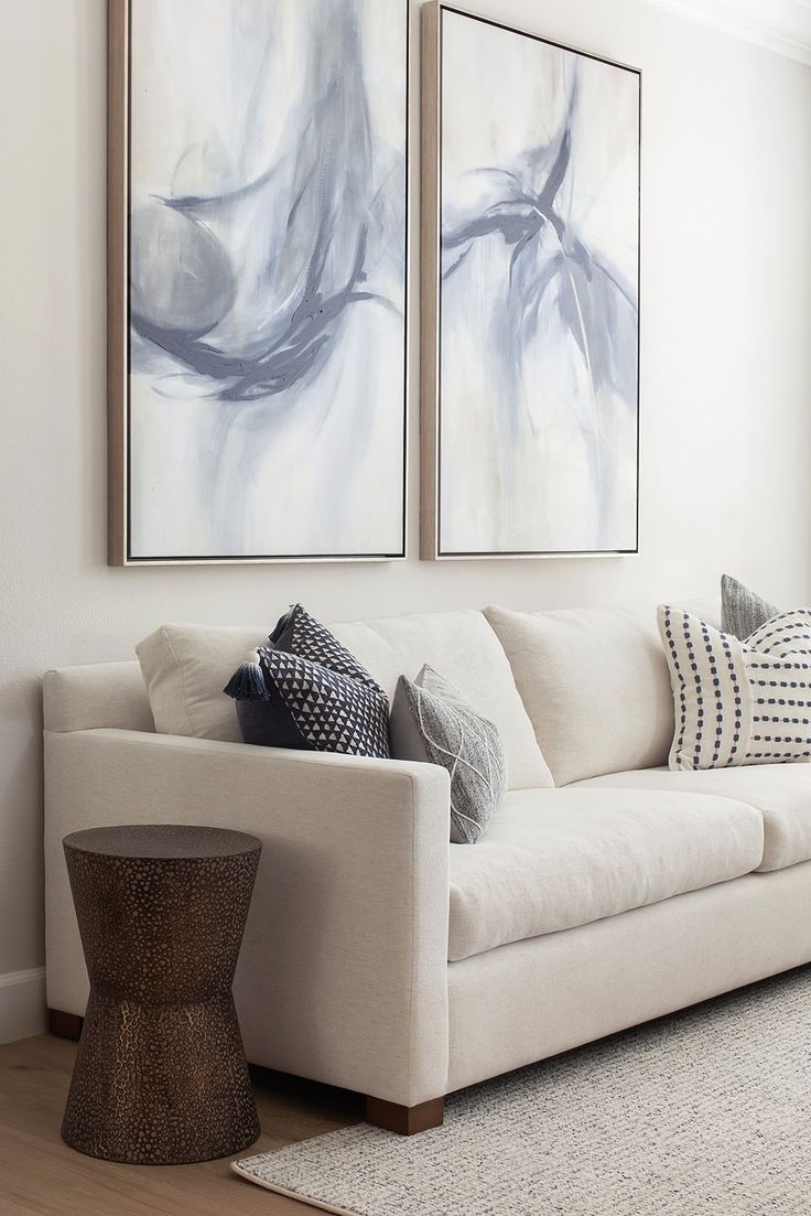 a living room with two paintings on the wall and a white couch in front of it