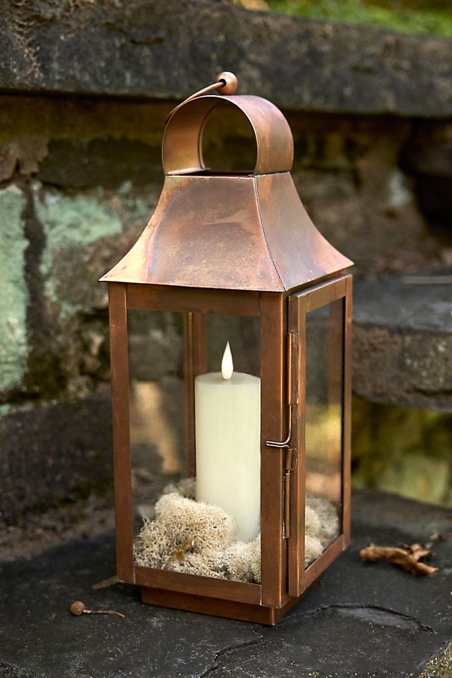 a candle that is sitting inside of a metal lantern on the ground next to some rocks