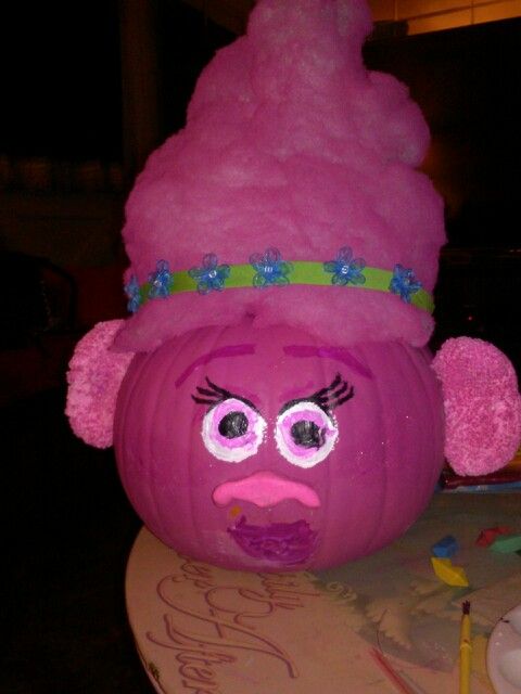 a purple pumpkin with a face painted on it's head and eyes, sitting on top of a table