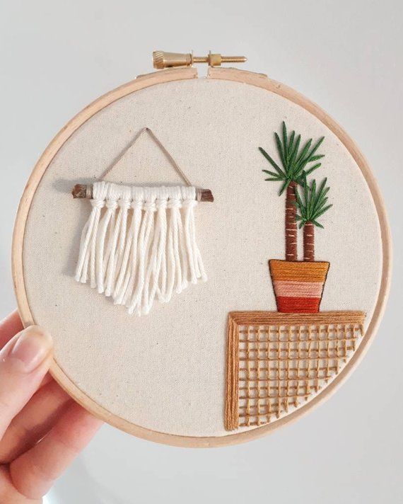 a hand is holding up a embroidery hoop with a plant and potted palm tree on it