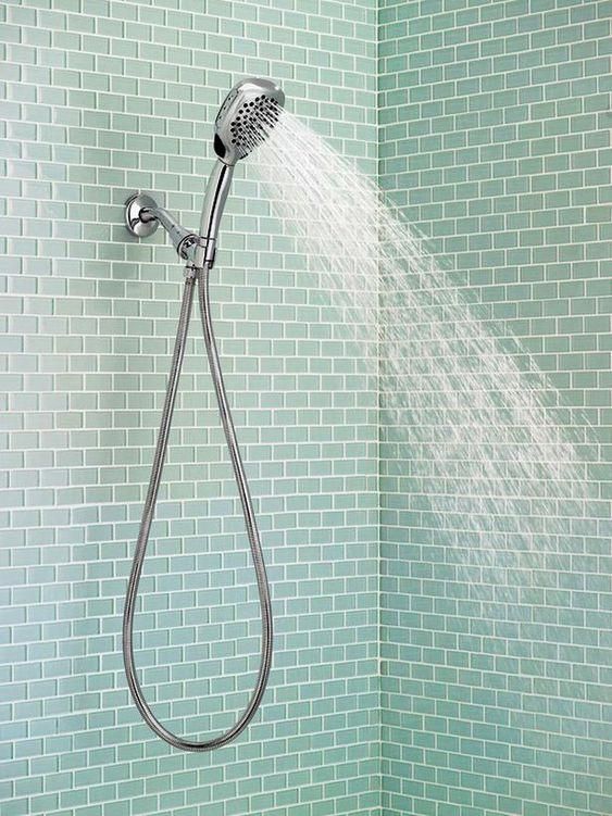 the shower head is spraying water from it's sprinkler in front of a tiled wall