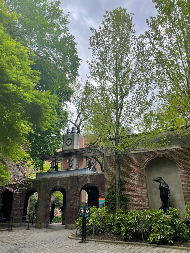 an old brick building surrounded by greenery and trees with a clock tower in the background