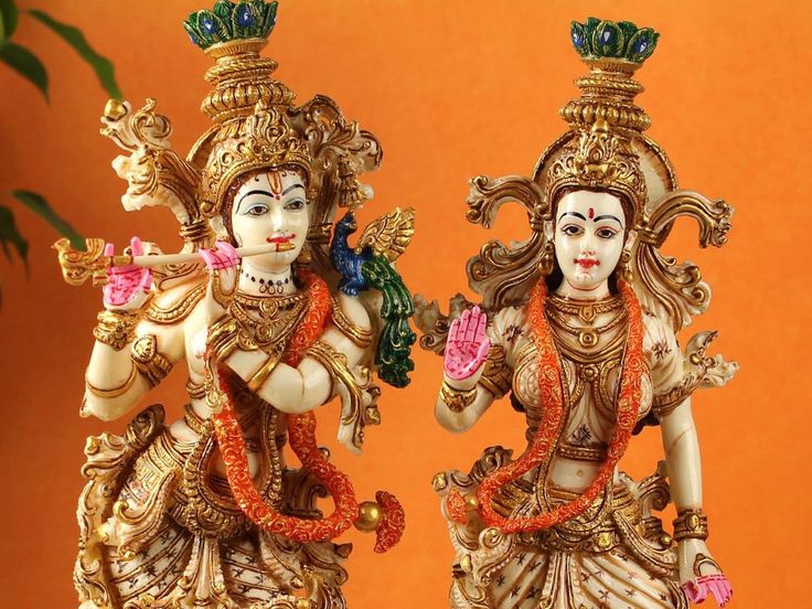 two statues of lord ganesh and goddess in front of an orange background with greenery