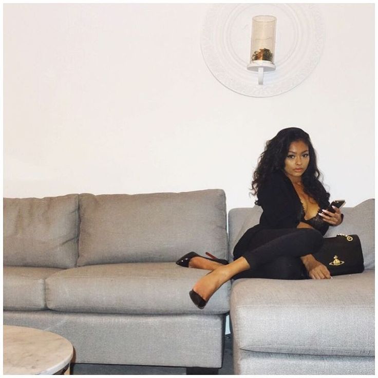 a woman sitting on top of a gray couch next to a coffee table and lamp