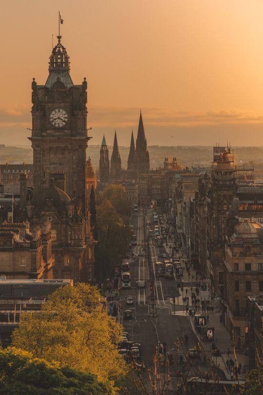 the sun is setting over an old city with tall buildings and a clock tower in the distance