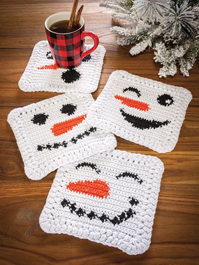 four crocheted coasters with faces on them and a cup of coffee in the middle