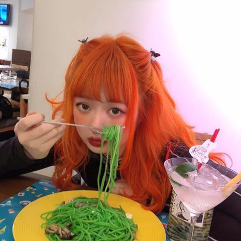 a woman with red hair eating noodles from a yellow plate