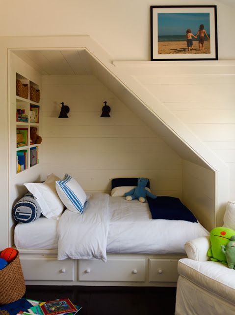 a bed sitting under a slanted ceiling next to a white chair and book shelf