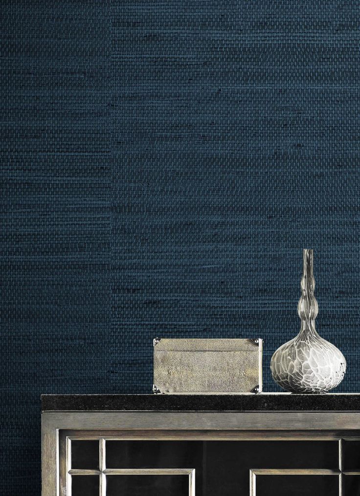 a silver vase sitting on top of a wooden table next to a blue wallpaper