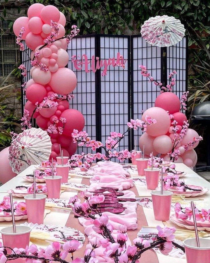 a table topped with lots of pink balloons and cups filled with drinks on top of it