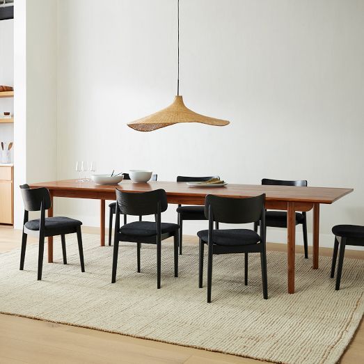 a dining room table and chairs in front of a white wall with an area rug on the floor