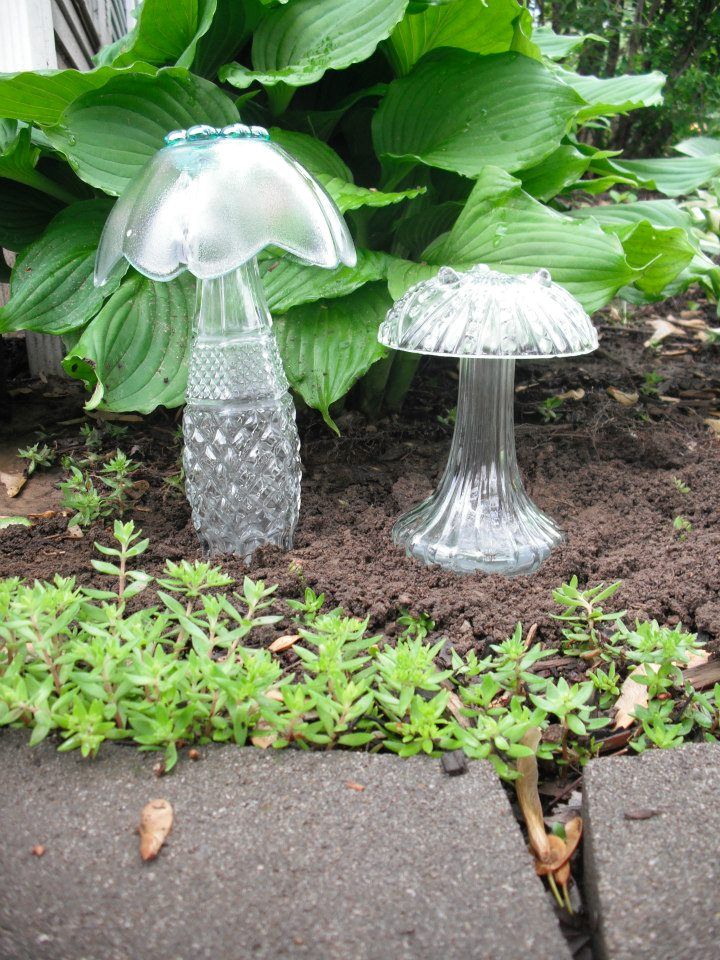 two clear glass vases sitting on the ground in front of some plants and bushes