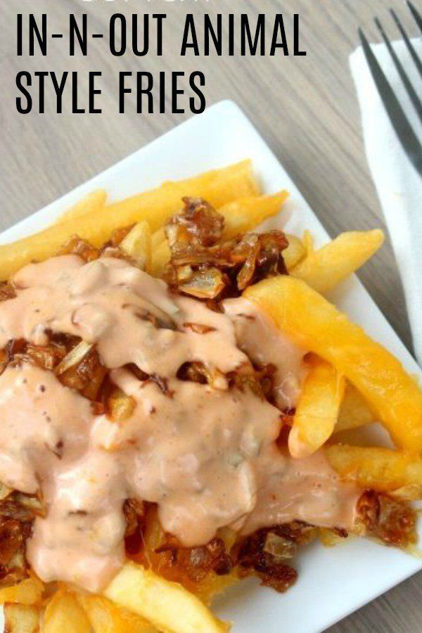 a white plate topped with fries covered in gravy next to a fork and knife