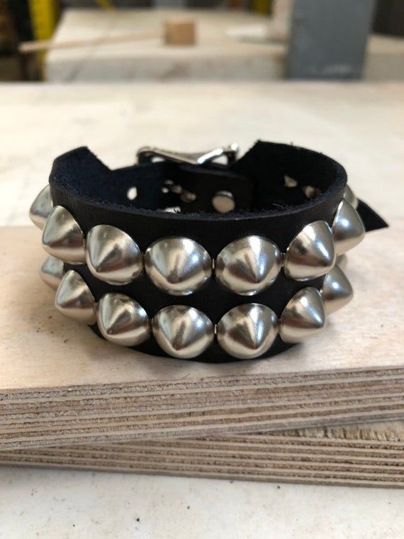 Classic studded punk bracelet with 2 rows of 1/2" cone studs. Fastens with a buckle and is adjustable. All hardware is nickle plated.Studs on black bracelets are nickel plated brass, studs on colored bracelets are nickel plated steel (old stock)Smaller bracelets have fewer studs per row.Made with hand dyed vegetable tan leather.Note: red bracelet is kind of pink-ish.Bracelet is 1.25" wide.Ask about custom sizing and color options! Punk Leather Bracelet With Studs For Festivals, Punk Style Studded Leather Bracelet For Festivals, Metal Leather Bracelet With Rivets For Festival, Adjustable Metal Bracelets With Studs, Rock Style Spiked Jewelry For Parties, Rock Style Party Jewelry With Spikes, Rock Style Spiked Party Jewelry, Punk Adjustable Cuff Bracelet With Rivets, Adjustable Punk Cuff Bracelet With Rivets