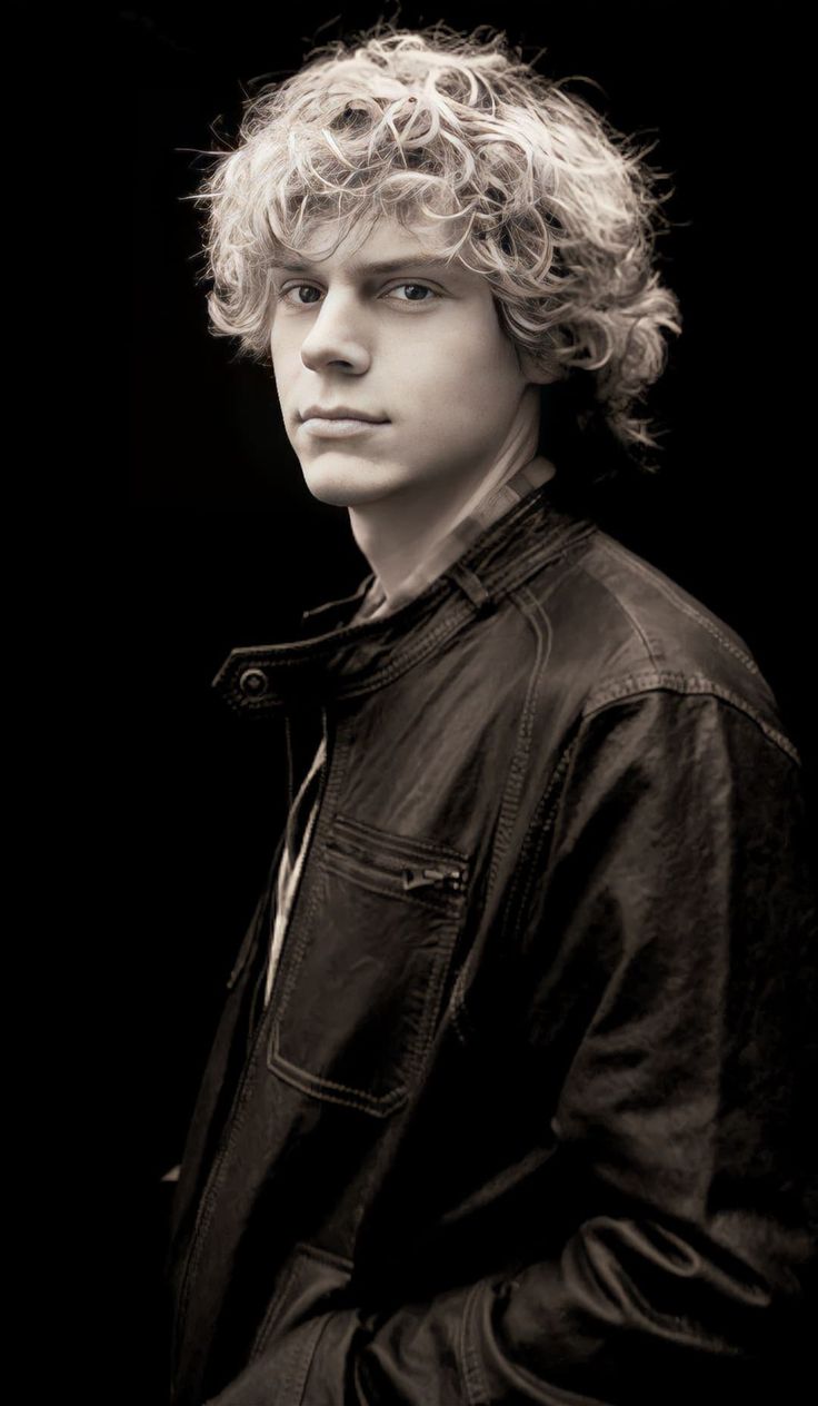 a black and white photo of a young man with curly hair wearing a leather jacket