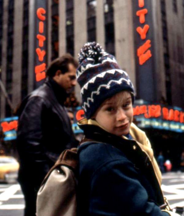 a young boy wearing a beanie standing in front of a tall building with the word new york written on it