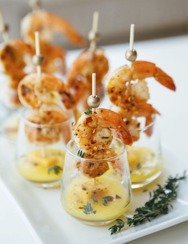 shrimp skewers are served in small glass cups with lemon sauce and herbs on the side