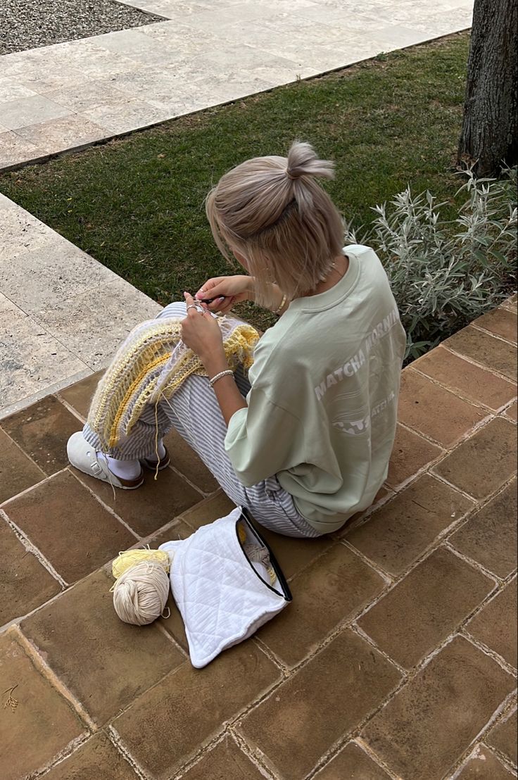 a woman sitting on the ground knitting