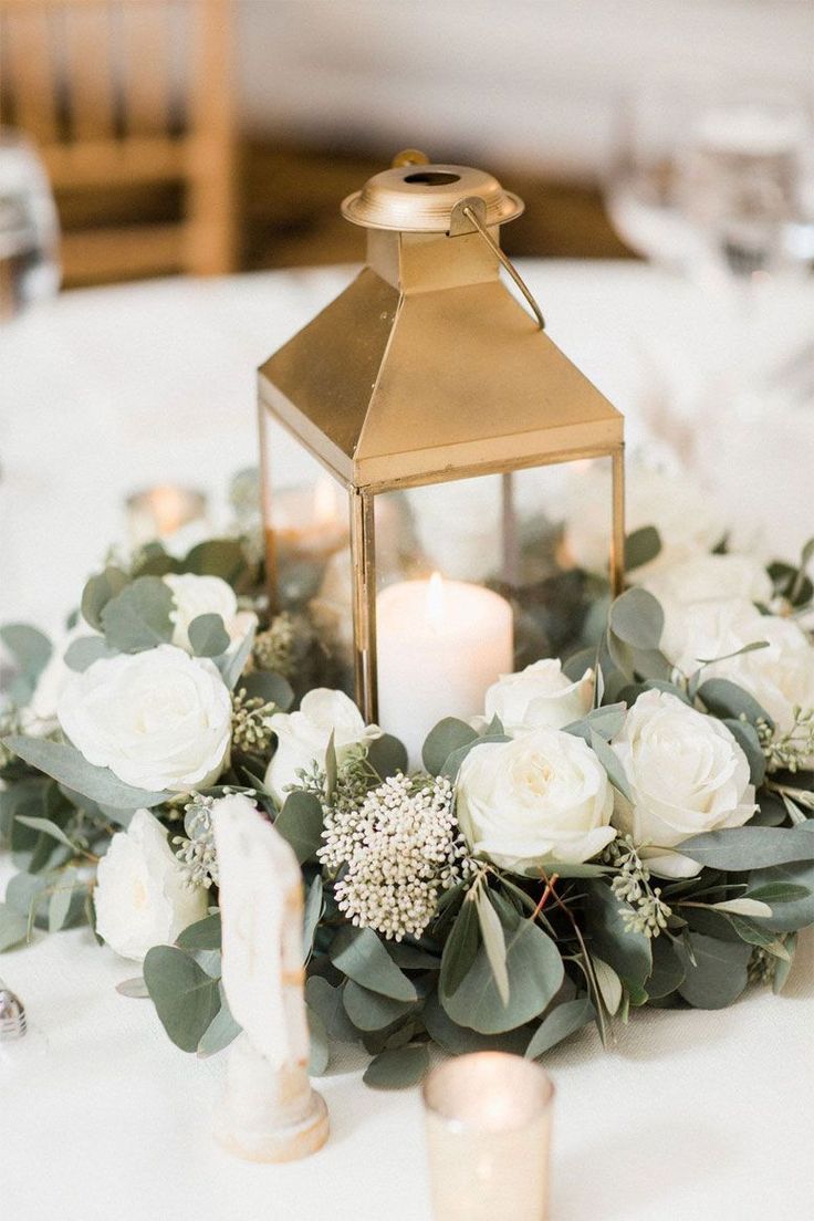 a lantern is on top of a table with white flowers and greenery around it