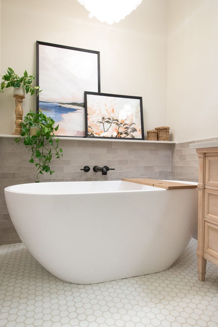 a white bath tub sitting in a bathroom next to a wooden dresser and potted plant