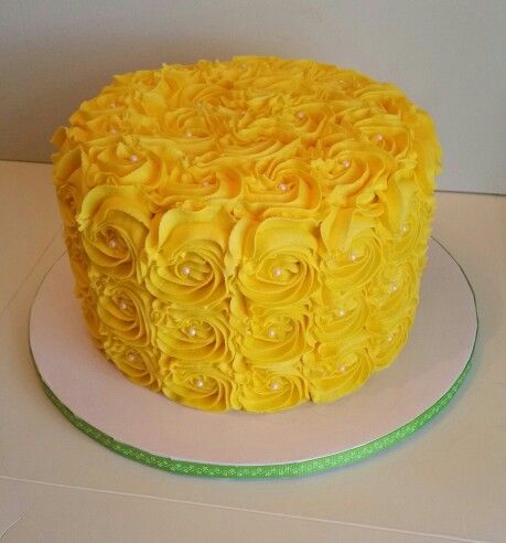 a cake with yellow frosting and roses on it sitting on a white plate next to a green ribbon