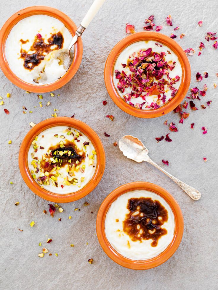 three orange bowls filled with yogurt and granola on top of a table