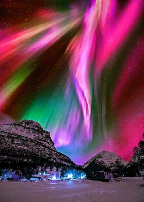 an aurora bore is seen in the sky above some mountains and trees, with bright colored lights