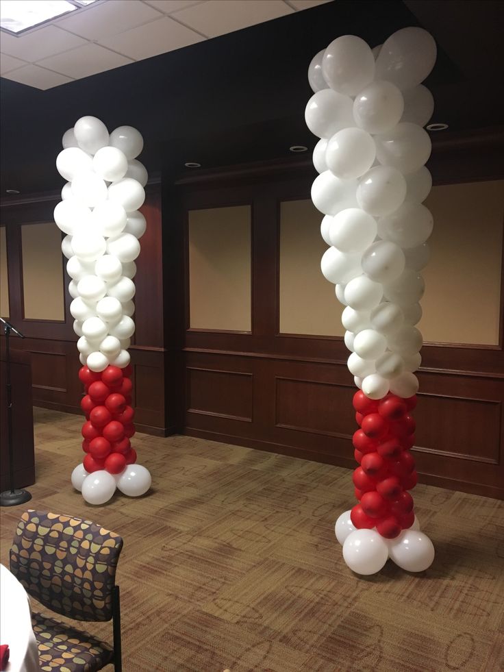 two tall red and white balloons in the shape of columns on a carpeted floor