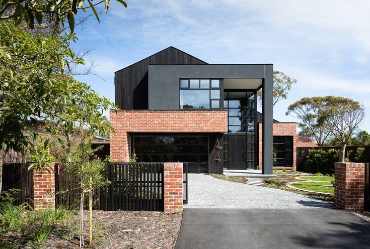 a modern house with brick walls and black iron gated driveway leading to the front entrance