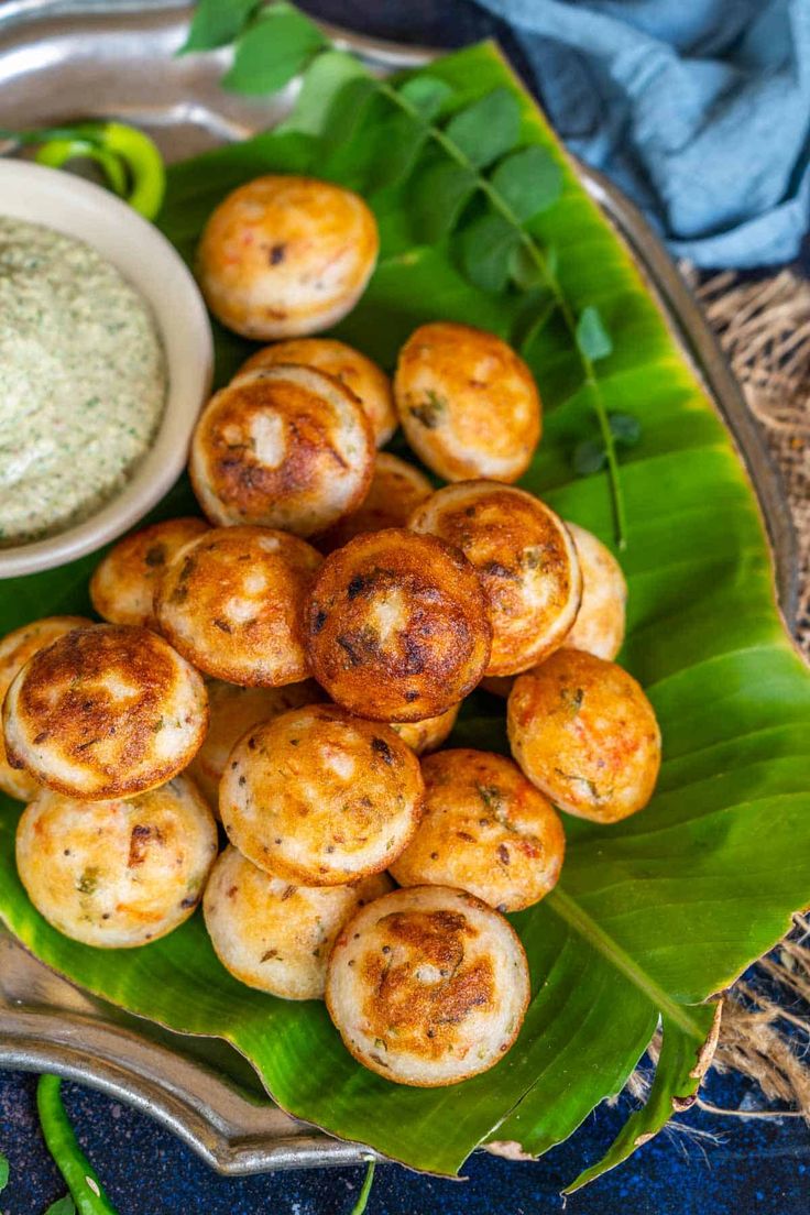 some food is sitting on a silver platter with green leaves and a small bowl