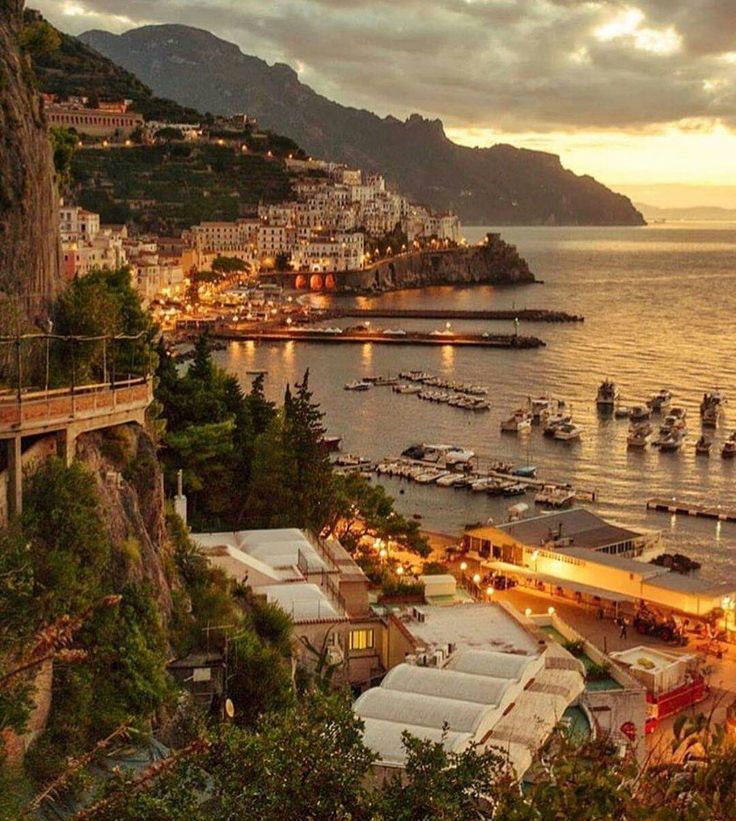 boats are docked in the water at dusk near a city on the shore and mountains