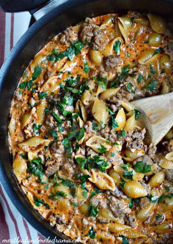 a skillet filled with pasta, meat and parsley on top of a table