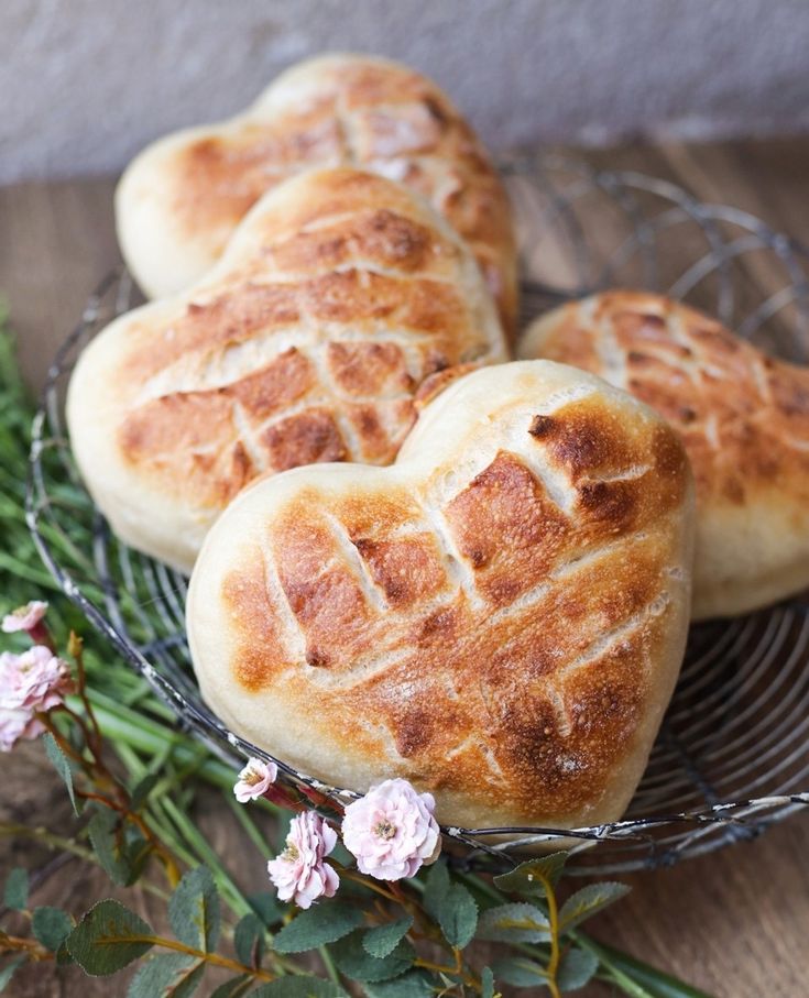 three heart shaped breads sitting on top of a wire rack next to flowers and greenery