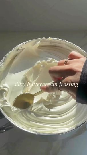 a person is holding a spoon in a bowl with white frosting on it,