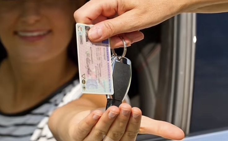 a woman holding up a car key to another person's hand and handing it out the window