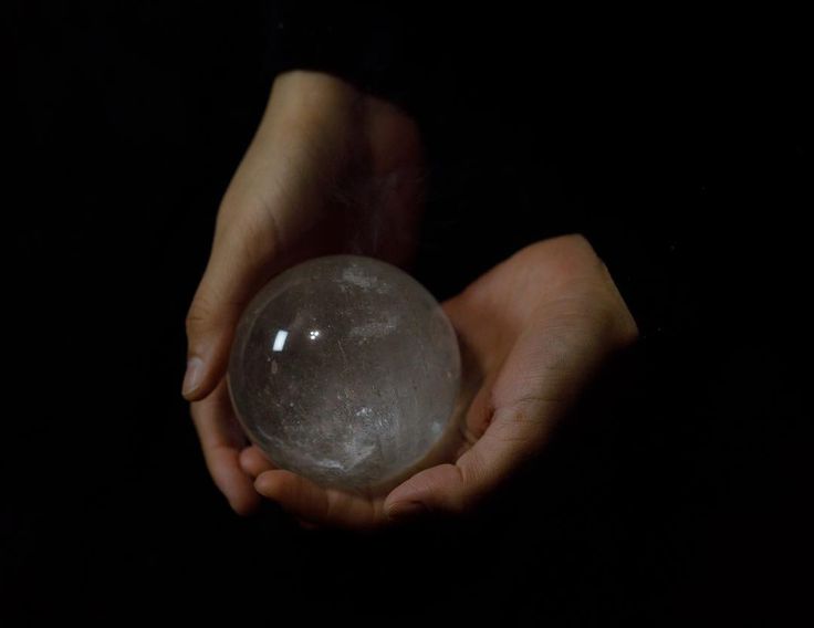 a person holding a crystal ball in their hands on a black background with the light shining through it