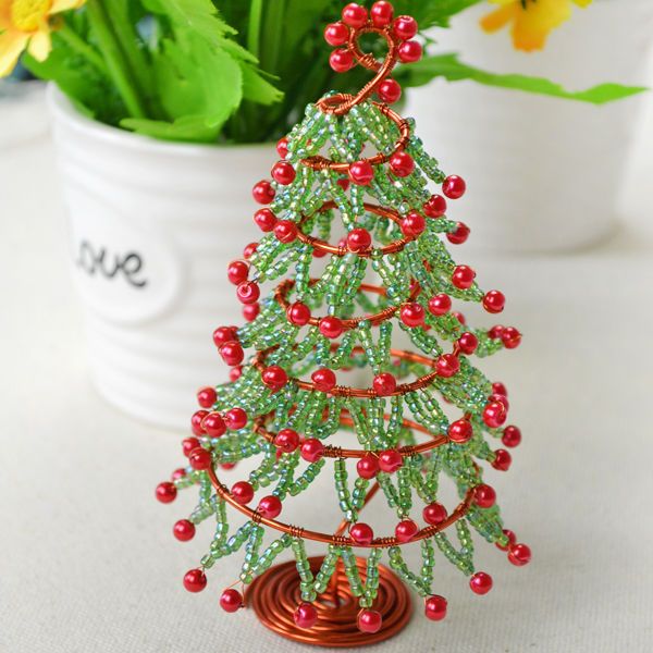 a small christmas tree made out of beaded beads and red berries sits next to a potted plant