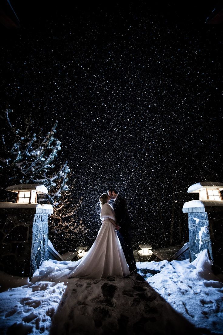 a bride and groom standing in the snow at night